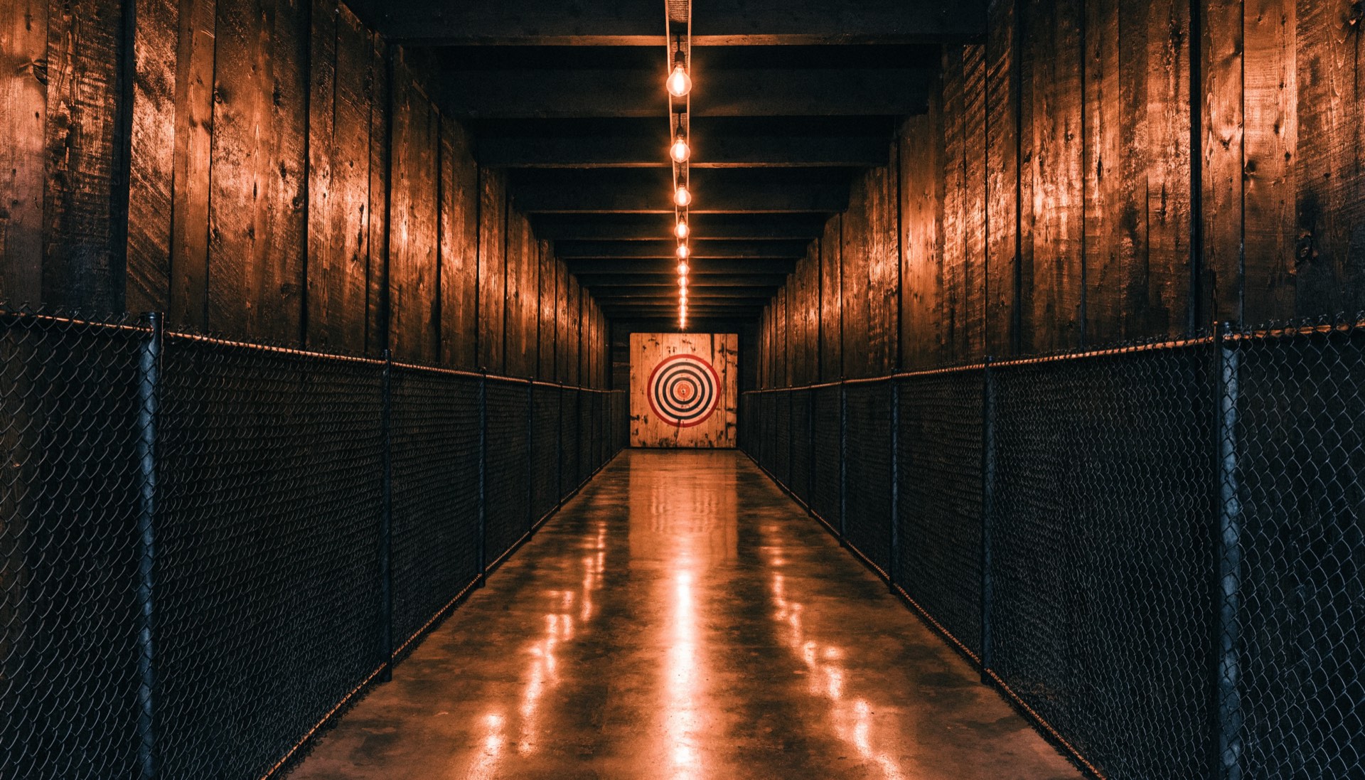 Looking down a caged axe throwing lane toward a lit target board
